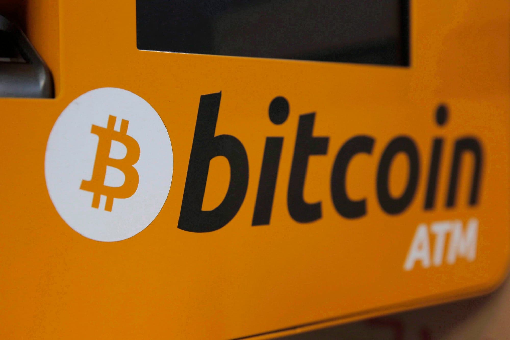 The bright yellow console of a Bitcoin ATM featuring a white and gold Bitcoin logo.
