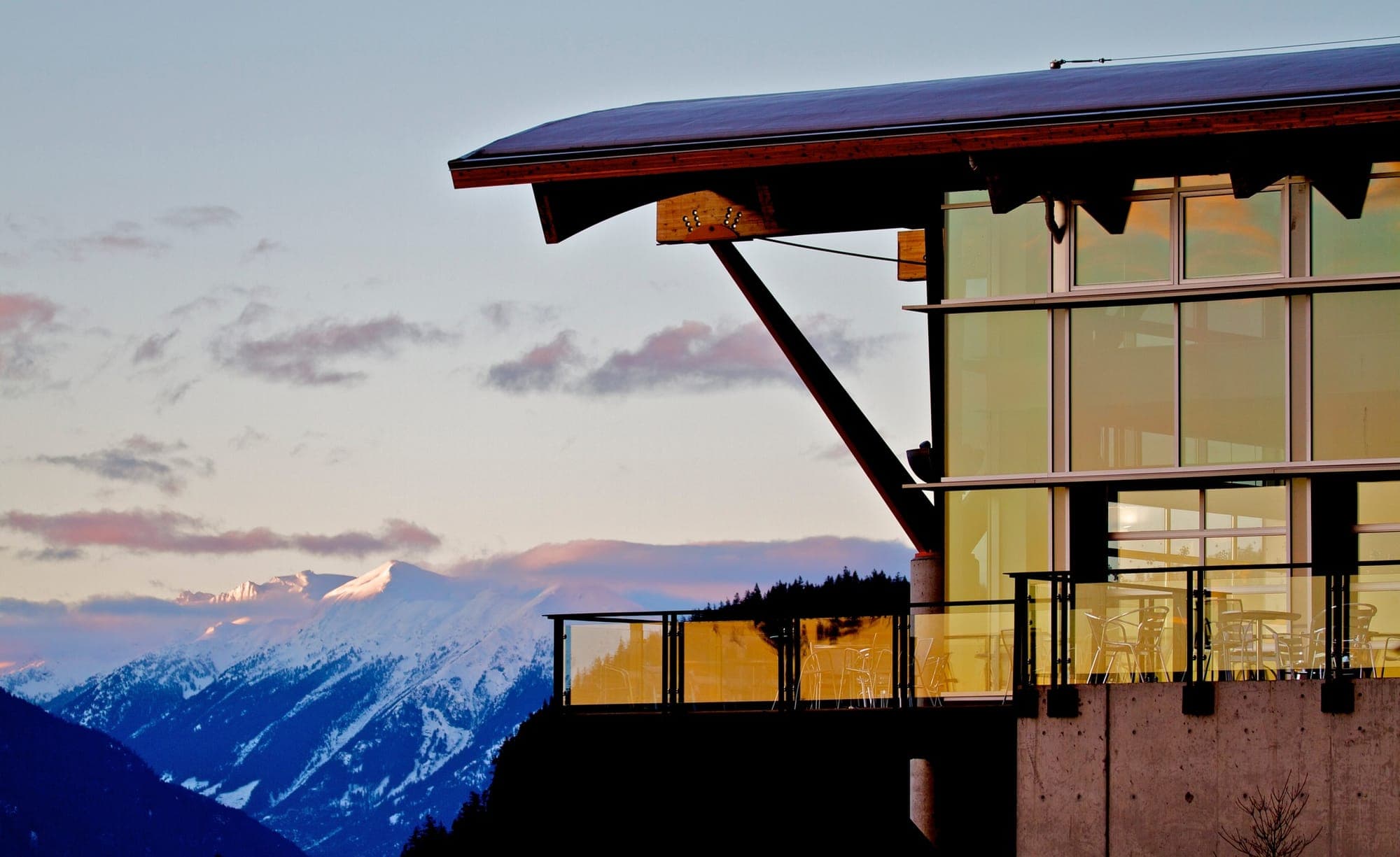 A glass-walled building at Quest University is shown, with snow-capped mountains in the background.