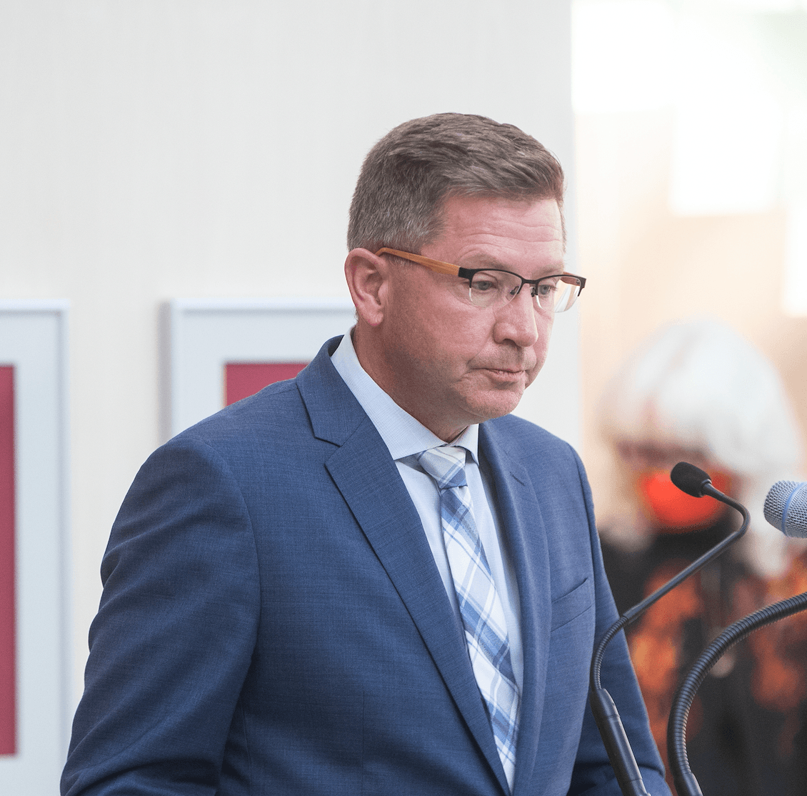 Man in blue suit stands in front of microphone.