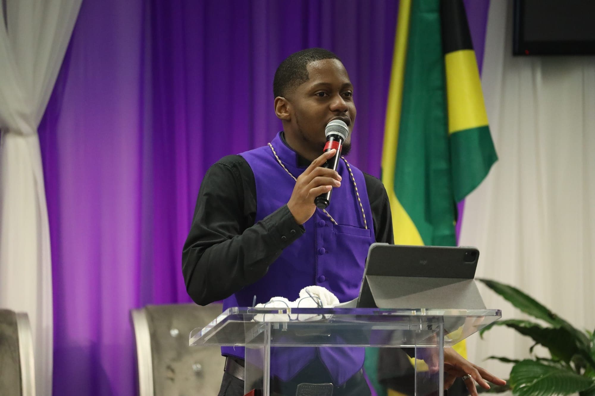 A pastor speaks into a microphone from behind a podium.
