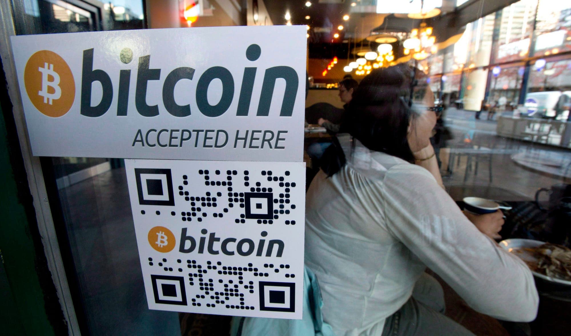 A sticker that says "Bitcoin Accepted Here" in the window of a coffee shop.