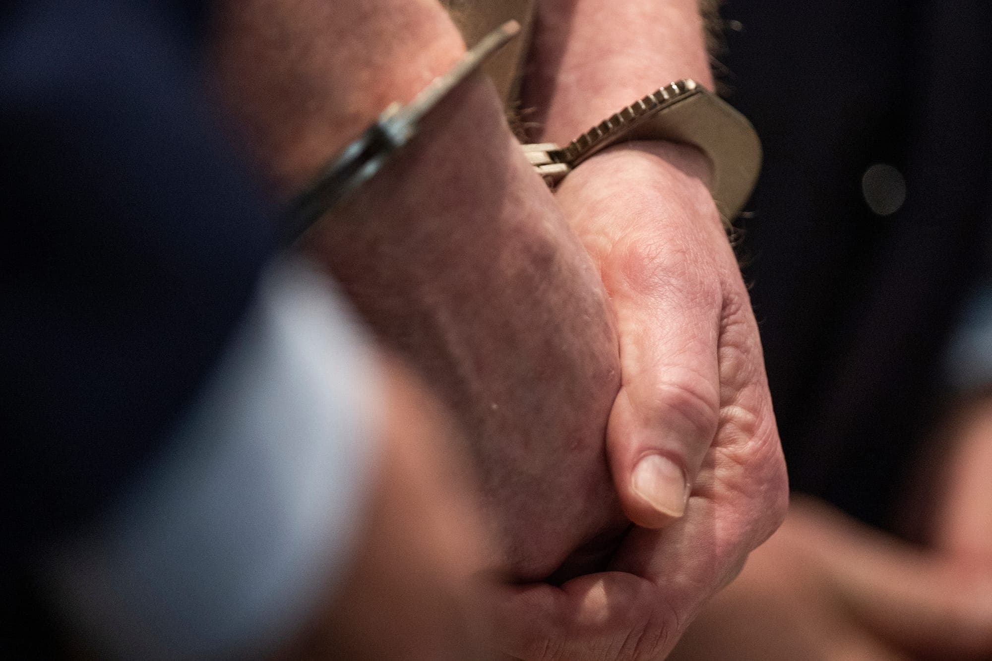 A pair of clasped hands wearing handcuffs are shown in close-up.