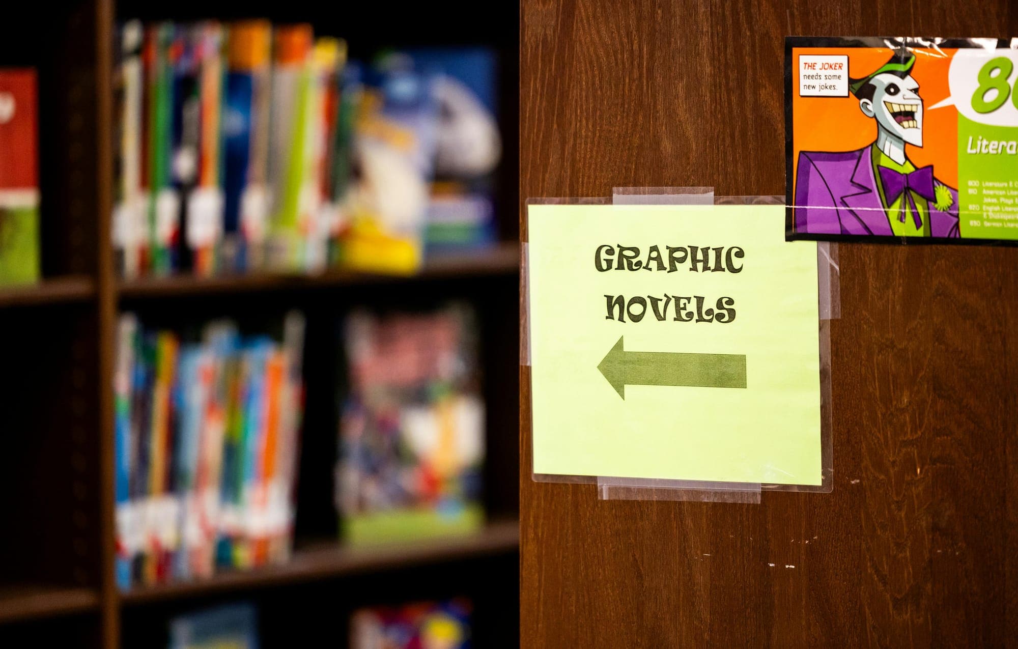 A sign on a library bookshelf reads "Graphic Novels" with an arrow pointing to the left.