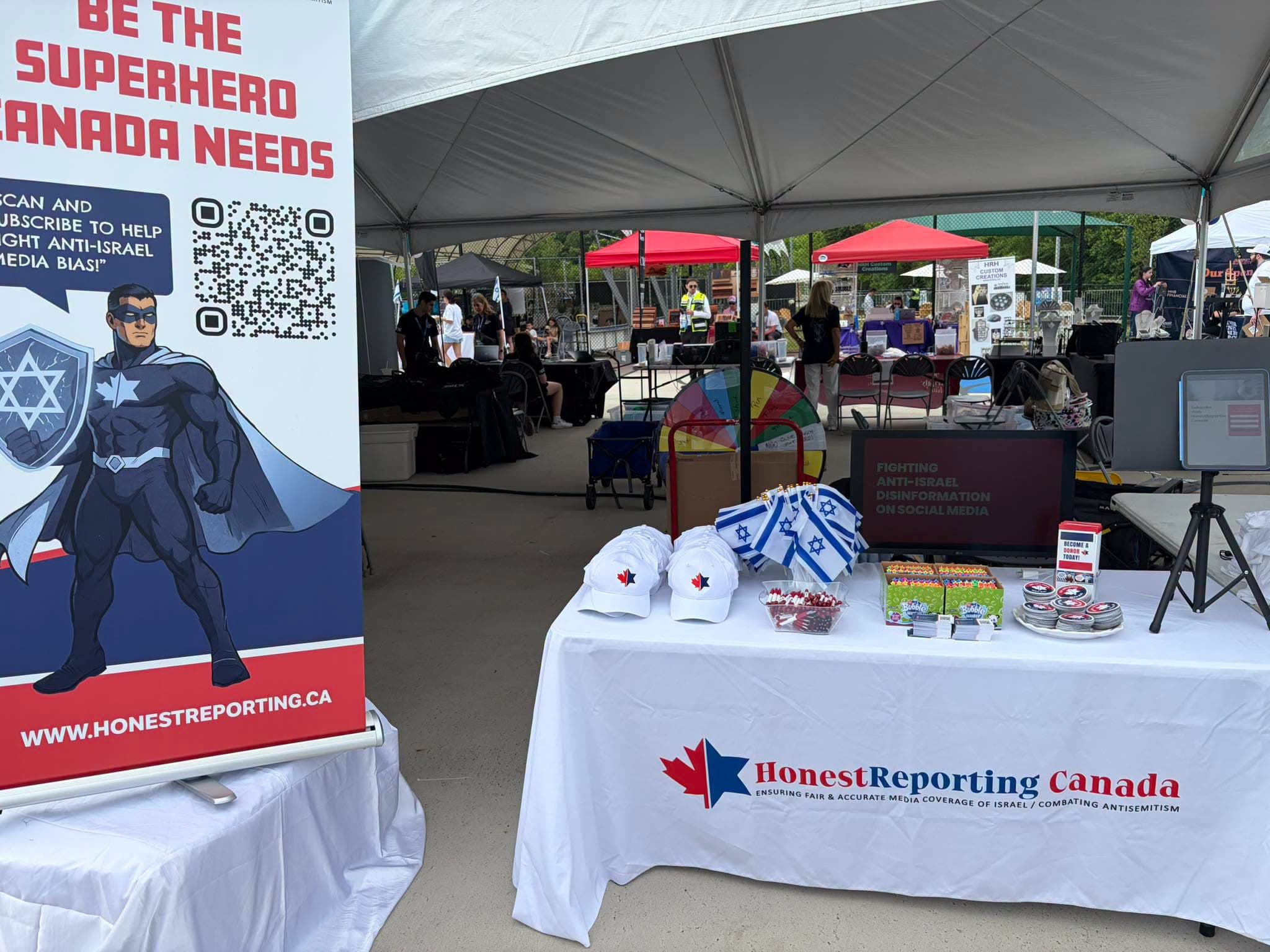 A table for Honest Reporting Canada is at an outdoor festival.