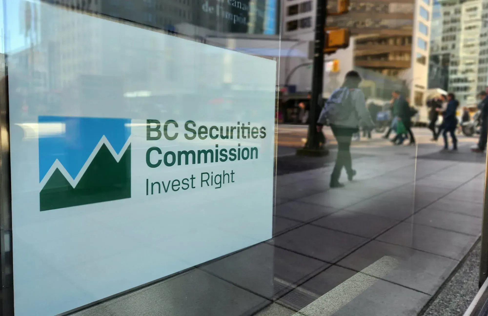 A white sign with the blue and green logo of the B.C. Securities Commission is pictured in a window in downtown Vancouver.