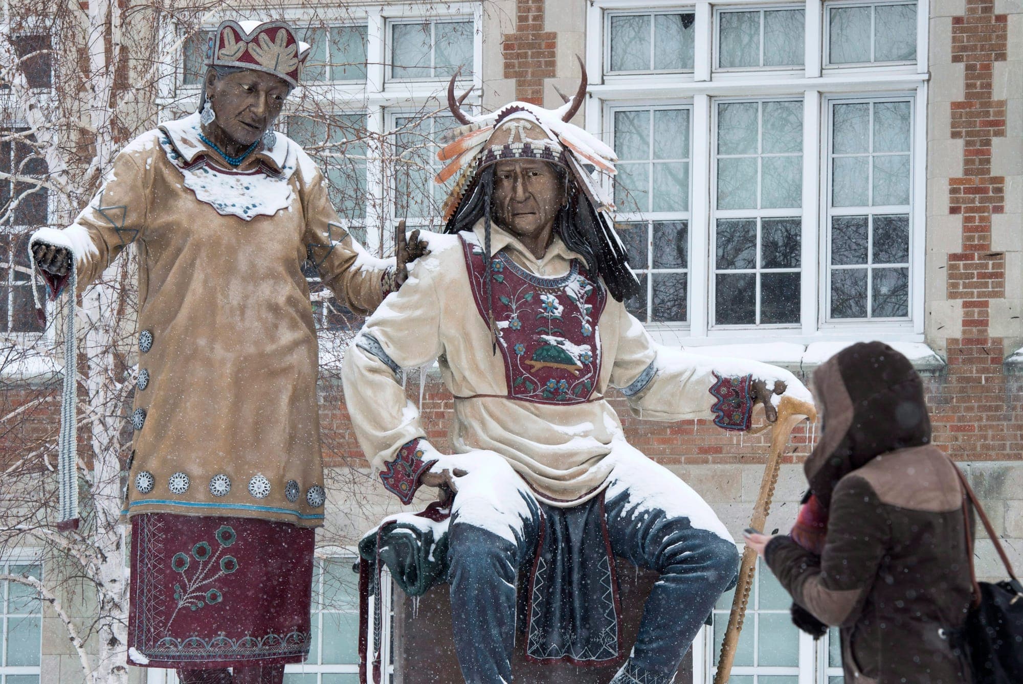 A woman walks past a snow-covered statue in 2015 in Montreal. The two figures of the statue portray the Kanien’kehà:ka (Mohawk) matrilineal tradition.