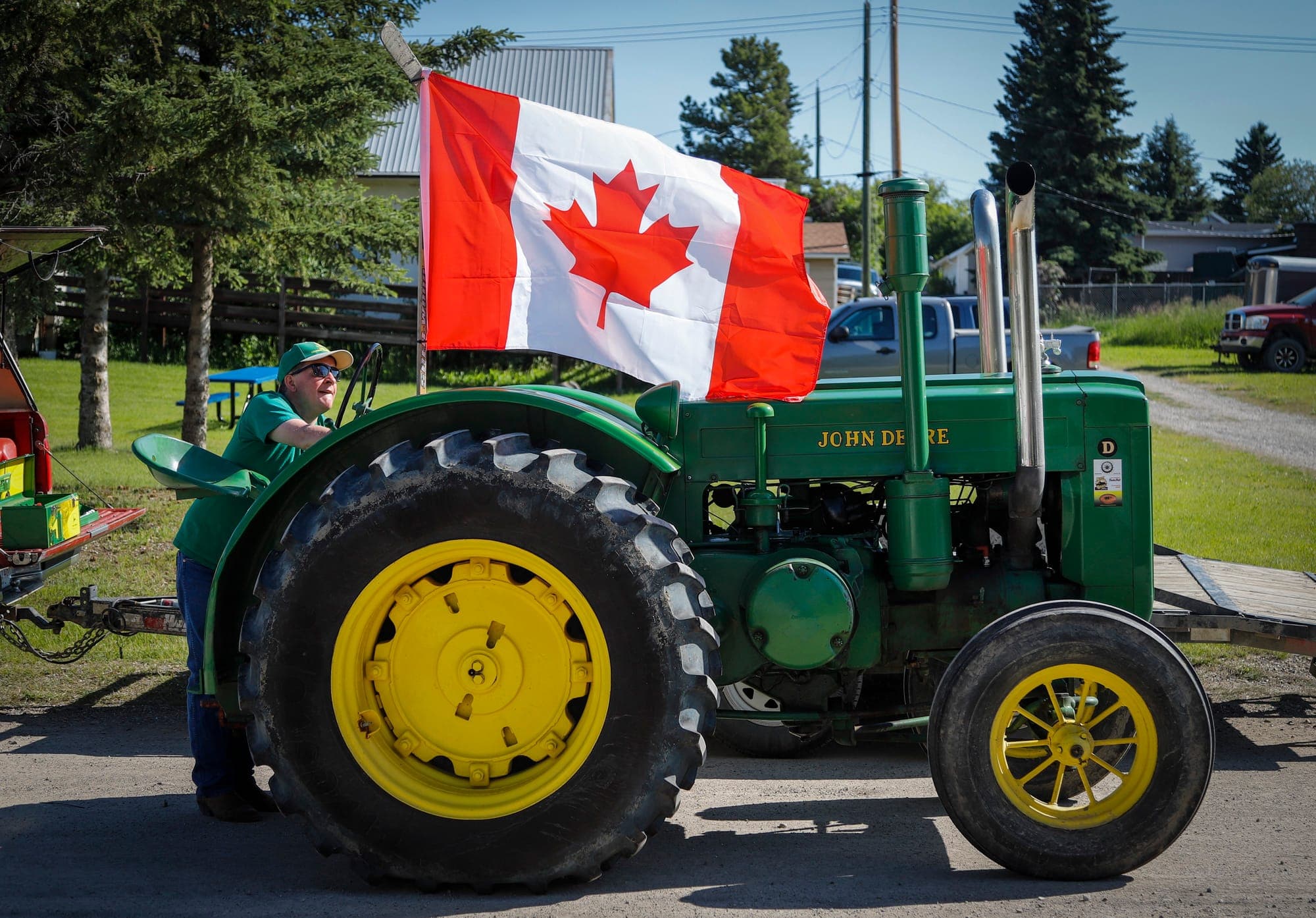 A man uses a hockey stick to attach a Canadian flag to his 1940 John Deere tractor.
