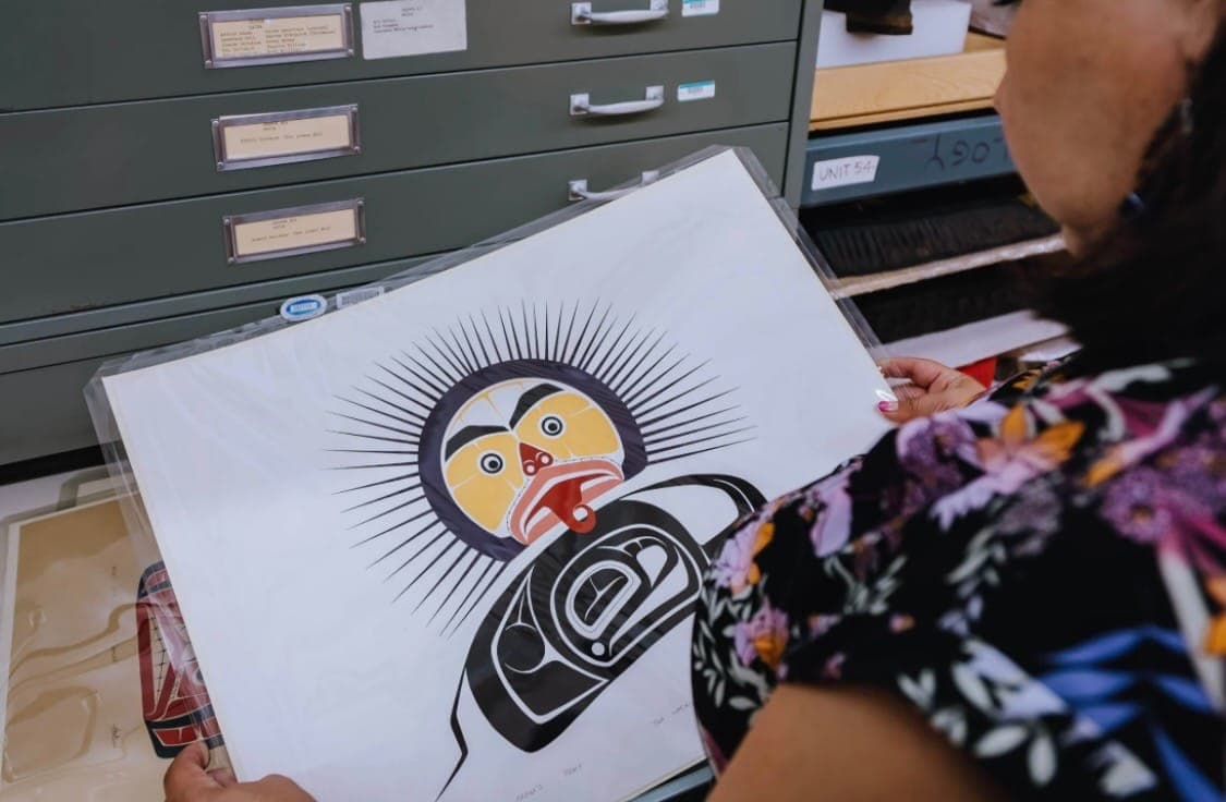 A woman viewed from behind holds an Indigenous print and artifact.