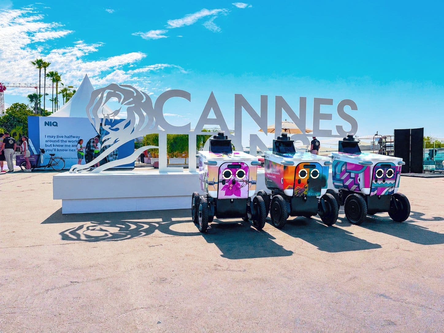 Three Serve Robotics robots, decked out in colourful designs, are photographed in front of the Cannes Lions festival in France.
