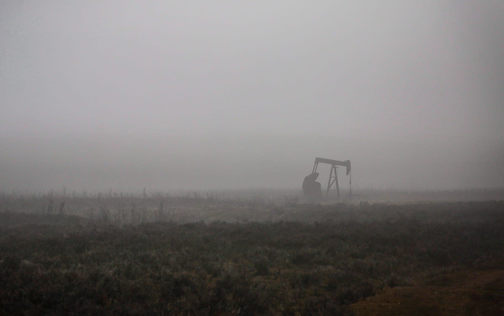 A pump jack in a field on a foggy, overcast day.