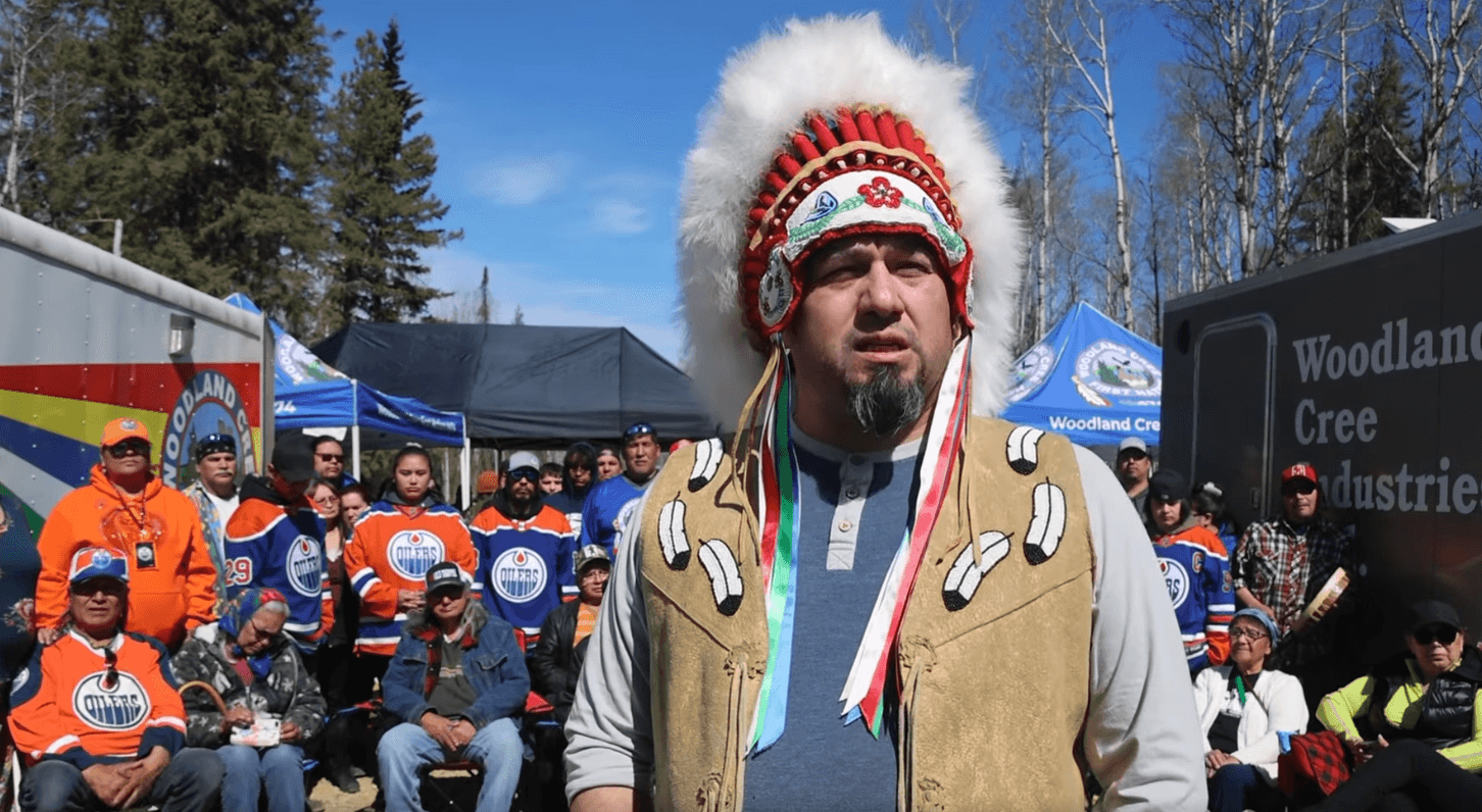Woodland Cree First Nation Chief Isaac Laboucan-Avirom is pictured speaking in front of a group of nation members wearing Edmonton Oilers jerseys.