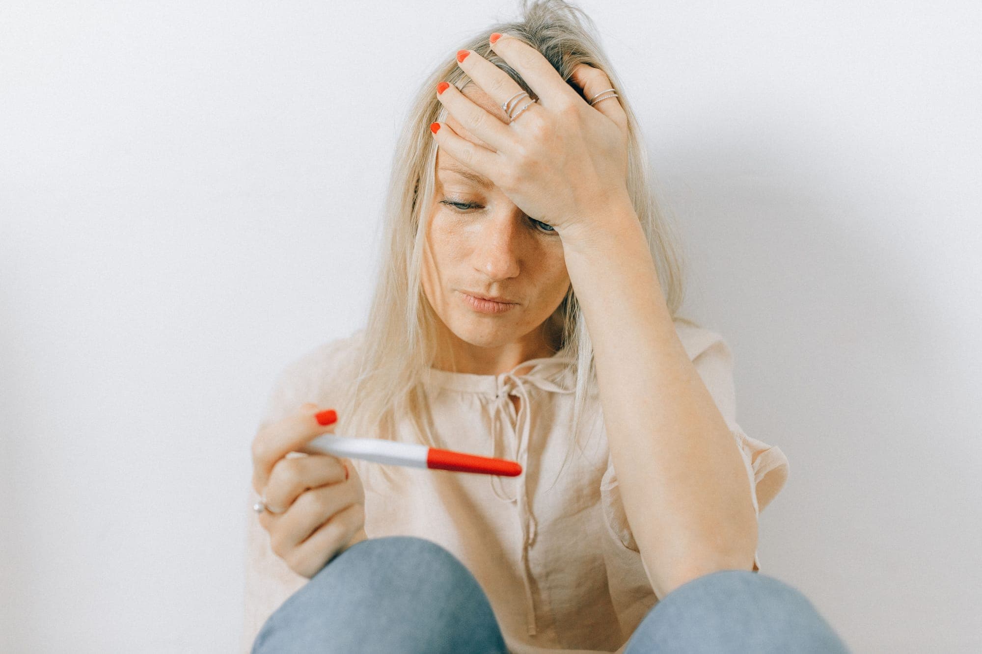 A blonde woman holds her head in her hands as she looks at a pregnancy test.