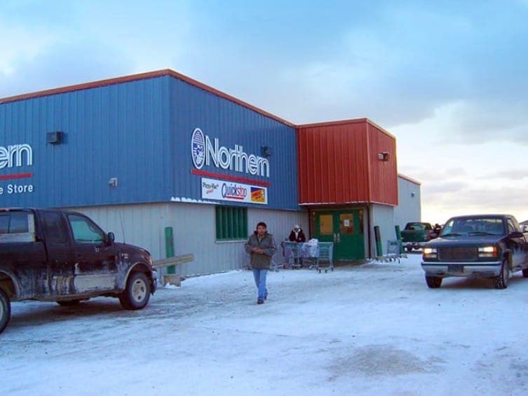 The Northern Store in Attawapiskat, Ont., with several vehicles parked outside the blue and red building on a snowy road.
