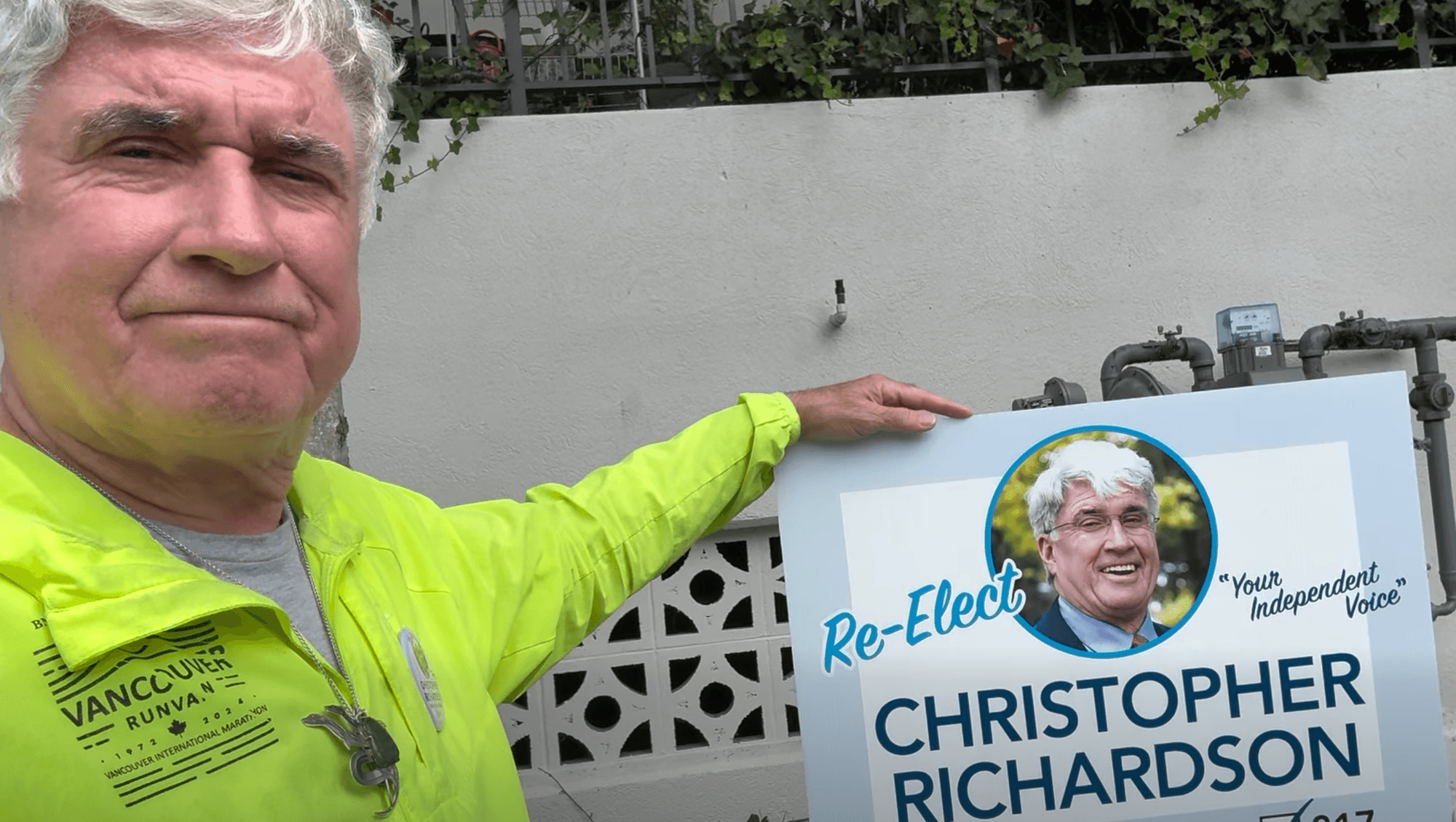 Christopher Richardson holds a sign saying 'Re-Elect Christopher Richardson: Your Independent Voice'